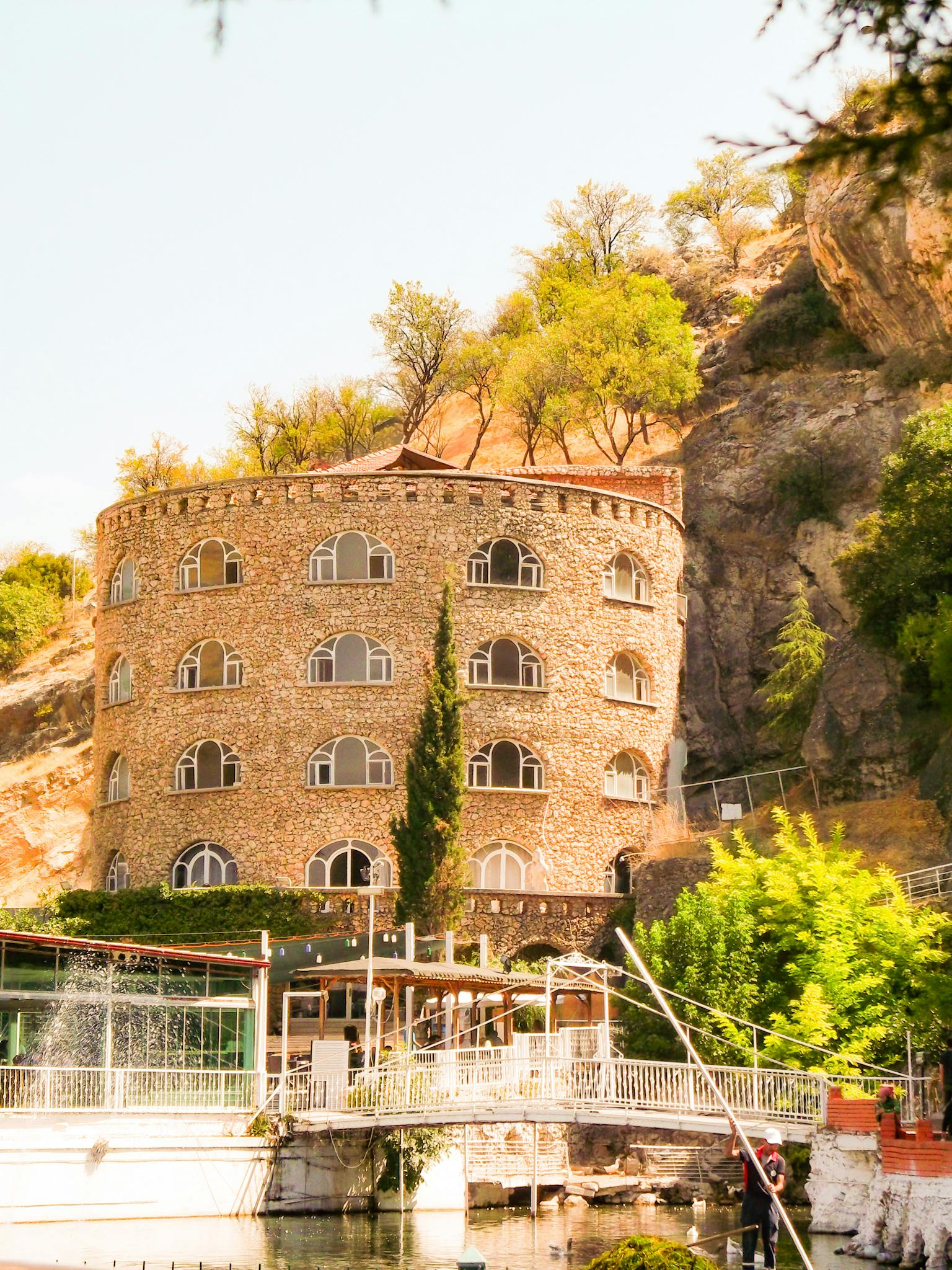 Stone hotel blends with rocky hillside, framed by lush greenery and sunny sky.